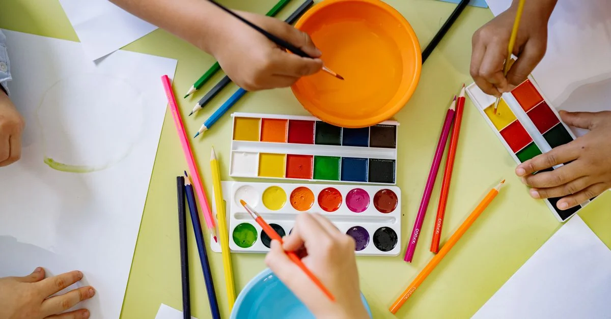 Des enfants utilisent des aquarelles et des crayons de couleur pour un projet artistique, favorisant la créativité.